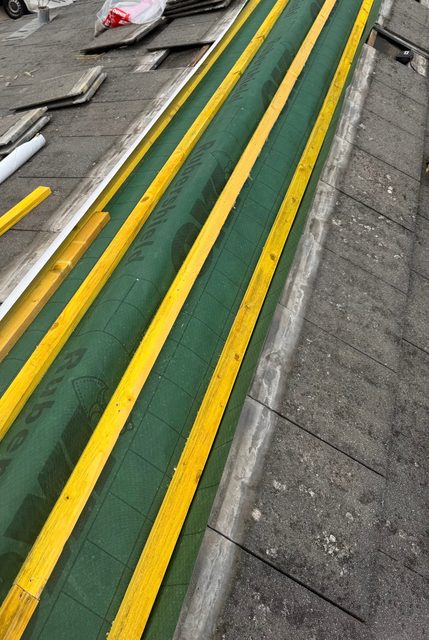 Storm Dry Roofing re-roof: yellow timber battens over green breathable membrane running alongside the old concrete tiles