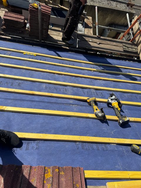 Storm Dry Roofing re-roof: rows of yellow battens fixed over blue breathable membrane, with roof tiles stacked ready at the top