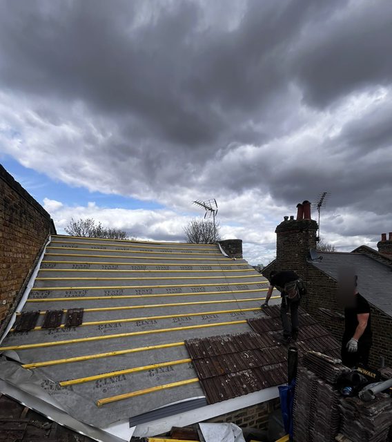 Storm Dry Roofing re-roof in progress: new breathable membrane and yellow battens across a stripped roof under a cloudy sky