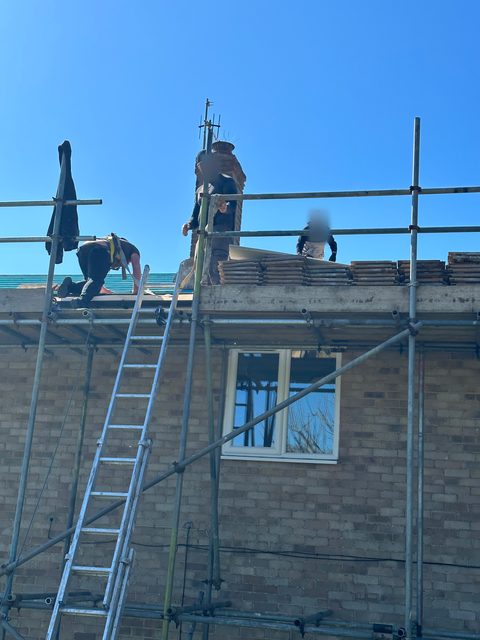Storm Dry Roofing crew on scaffold stripping the old tiles off a roof, with tiles stacked along the top