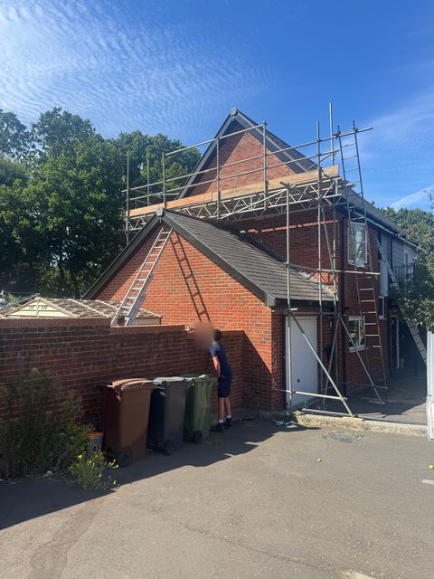 Storm Dry Roofing scaffold put up round a brick gable end and porch roof, with ladders up to the roof