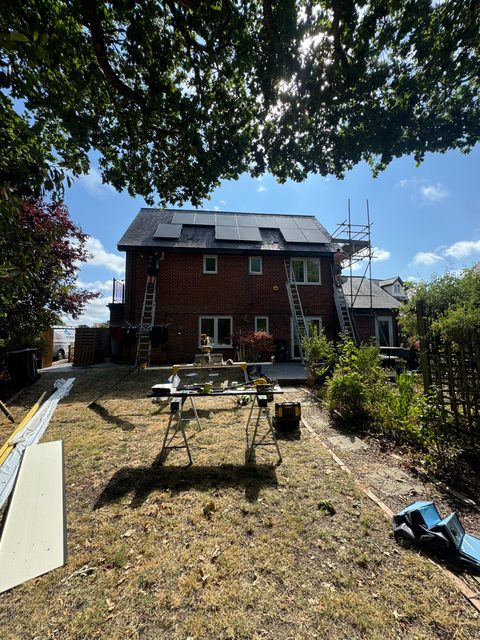 Storm Dry Roofing: ladders and a scaffold tower up at the back of a brick house with solar panels, with work benches set up in the garden